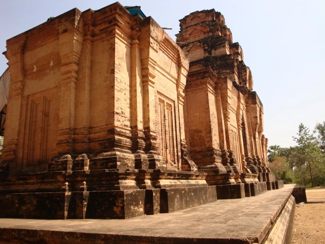 Verfallene rötliche Ziegelsteinmauern historischer Tempelanlage mit mehreren Türmen und Säulen, Sonnenlicht beleuchtet Architektur
