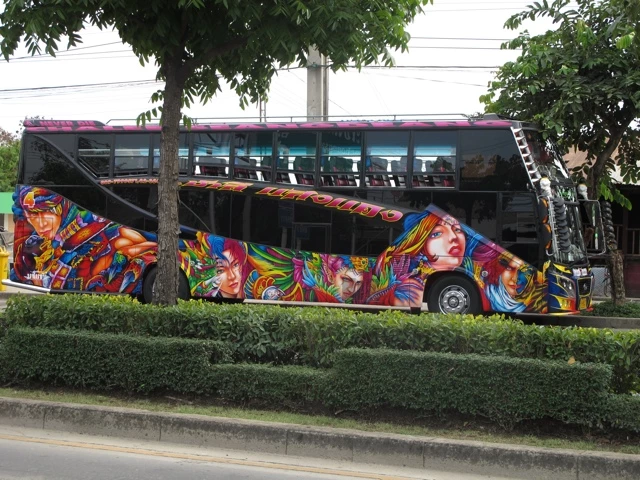 Großer Reisebus mit farbenfroh gestalteter Seitenwand, verziert mit bunten Graffiti-Porträts in Regenbogenfarben, geparkt neben Hecken