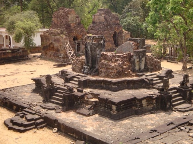 Verfallene Steinruinen eines antiken Tempels mit mehrstufigen Plattformen und Mauerfragmenten, umgeben von Bäumen