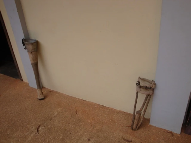 Zwei veraltete, hölzerne Beinprothesen an einer beigen Wand, auf einem braunen Untergrund stehend