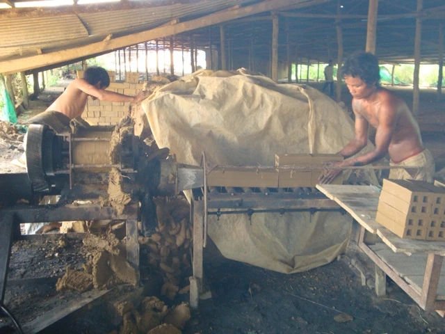 Zwei Männer arbeiten an einer Maschine zur Herstellung von Lehmziegeln in einer offenen Werkstatthalle