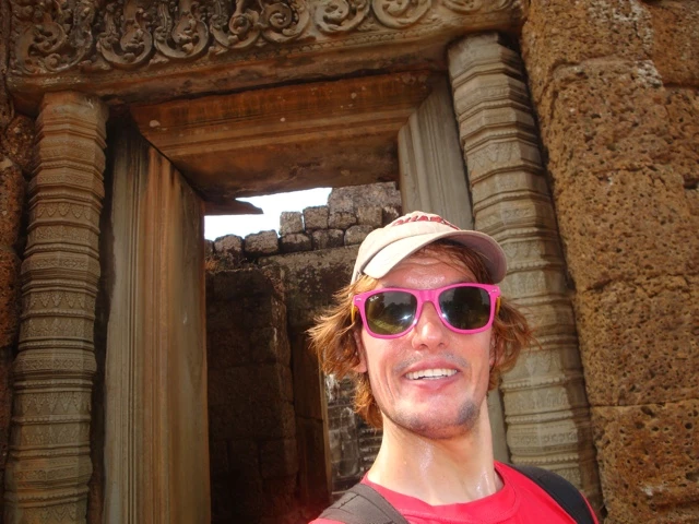 Lächelnder Tourist mit rotem T-Shirt und pinkfarbener Sonnenbrille steht in historischem Steinportal von Angkor