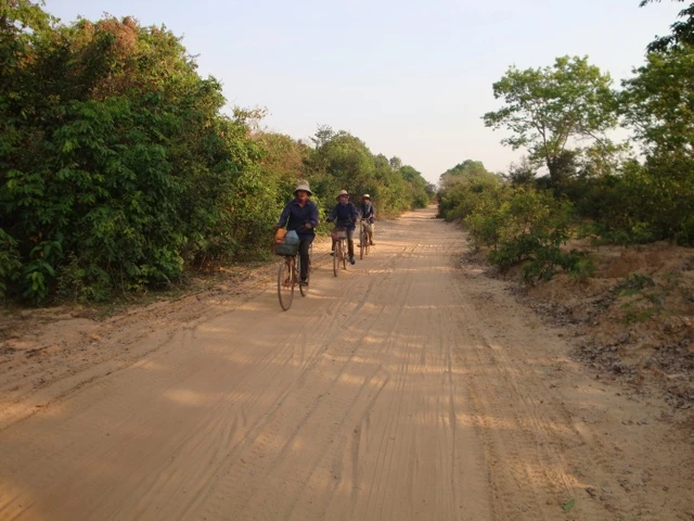 Drei Radfahrer auf staubiger Sandstraße, umgeben von Bäumen und Sträuchern in Kambodscha