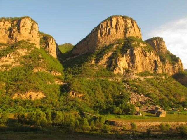 Steile Felswände mit grüner Vegetation im Vordergrund, Sonnenlicht beleuchtet Berge in warmem Gelb-Orange