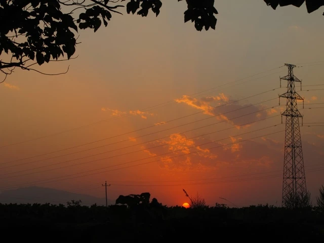 Orangefarbener Sonnenuntergang mit Silhouetten von Strommasten, Bäumen und Landschaft im Vordergrund