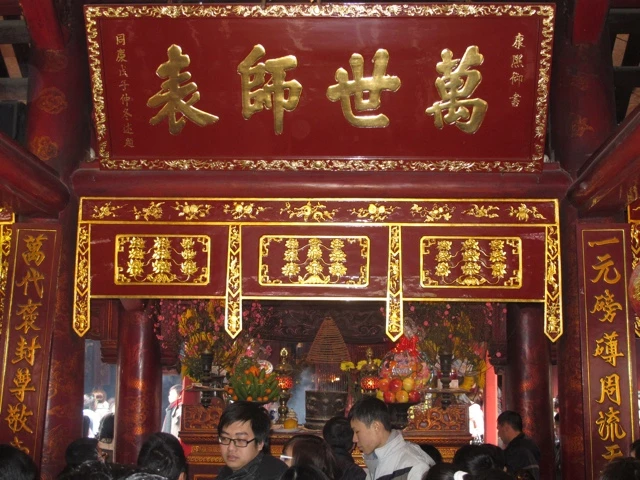 Rot-goldener Altarraum mit traditioneller chinesischer Schrift, Opfergaben und Besuchern im Vordergrund