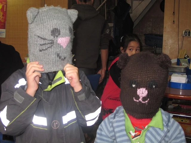 Zwei Kinder tragen handgestrickte Masken - eine graue Katze und eine braune, vermutlich Bären-Maske