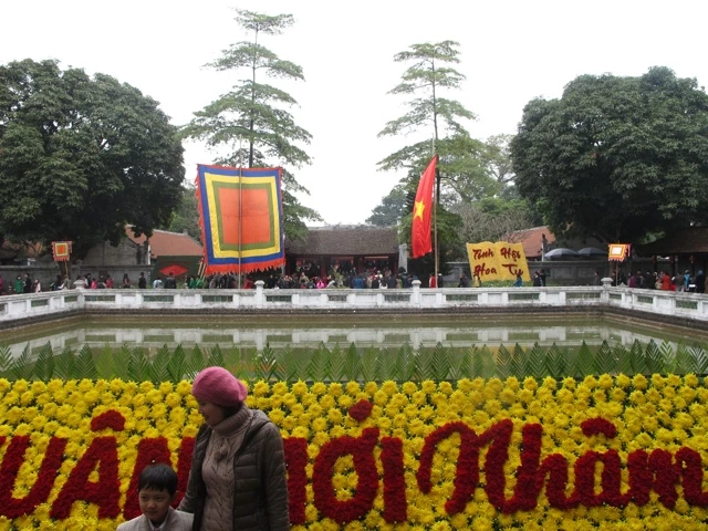 Große Blumenkomposition aus gelben und roten Blüten mit einem Teich im Hintergrund, traditionelle vietnamesische Flagge und Bäume