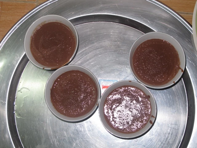 Vier braune Desserts in grauen Förmchen auf einem großen Metalltablett, unterschiedlich glänzend und strukturiert