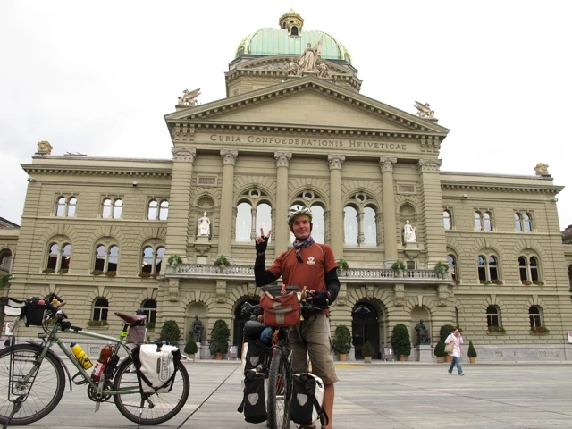 Fahrradreisender mit Touren-Rad vor historischem Bundeshaus in Bern, grüne Kuppel im Hintergrund