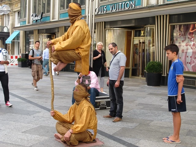 Zwei Performer in gelben Ganzkörperanzügen als lebende Statuen auf Münchner Straße vor Luxusgeschäft