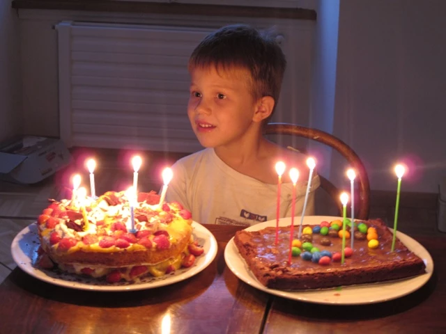 Zwei Geburtstagstorten mit brennenden Kerzen, ein lächelnder Junge im Hintergrund