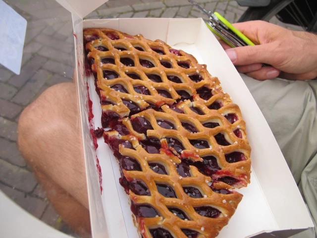 Aufgeschnittener Kirschkuchen mit goldenem Gitterdeckel in weißer Kartonschachtel, teilweise angeschnitten