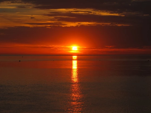 Dramatischer Sonnenuntergang über ruhiger Wasserfläche, orangerot leuchtender Himmel spiegelt sich im glatten Gewässer