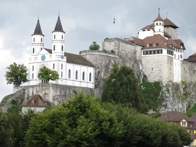 Historische Burganlage mit weißer Kirche und Steinmauern, auf steilem Felsen thronend, umgeben von grünem Baumbestand