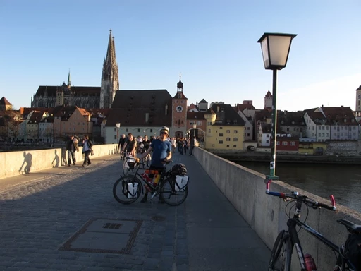 Fahrradfahrer auf historischer Steinbrücke mit gotischem Dom und mittelalterlicher Altstadt von Regensburg