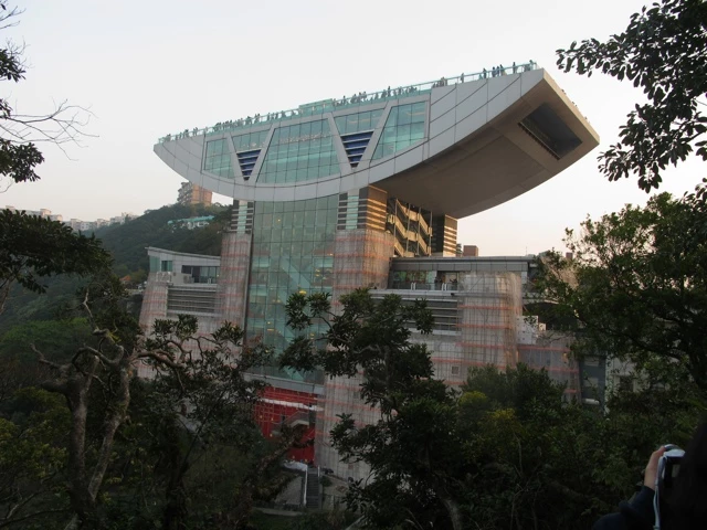Futuristisches Hochhaus mit auskragendem Glasanbau, umgeben von Bäumen und Vegetation in Hongkong