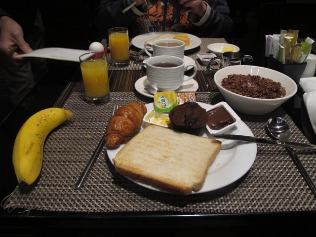 Gedeckter Frühstückstisch mit Kaffee, Orangensaft, Croissant, Toast, Banane und Schokolade