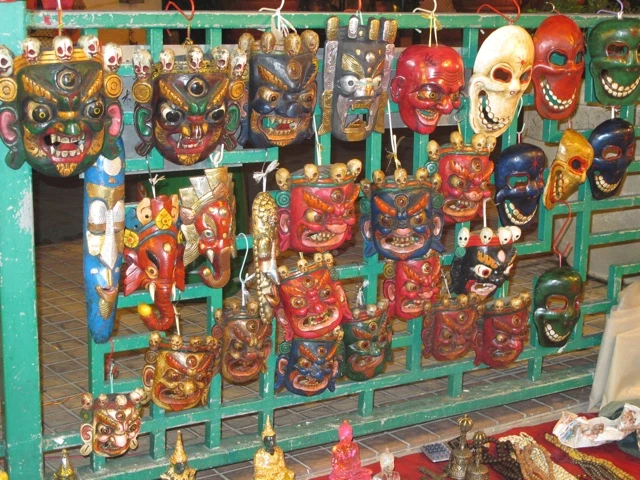 Mehrere Dutzend handgeschnitzte, traditionelle Masken in leuchtenden Farben wie Rot, Blau und Gelb an einem grünen Gitter aufgehängt