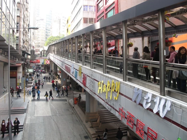 Moderne Fussgängerbrücke in belebter Stadtlandschaft Hongkongs mit Rolltreppe und Passanten