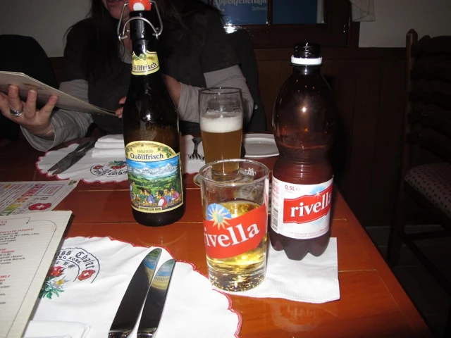 Zwei Flaschen Rivella und eine Bierflasche auf einem gedeckten Holztisch mit Servietten und Besteck