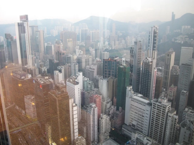 Blick auf eine dicht bebaute Skyline mit zahlreichen Hochhäusern und Wolkenkratzern in Hongkong, umrahmt von Bergen im Hintergrund
