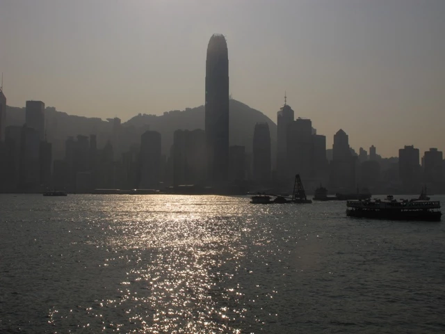 Silhouette von Hongkongs Wolkenkratzern bei Sonnenuntergang, Blick über glitzerndes Wasser mit Booten im Vordergrund