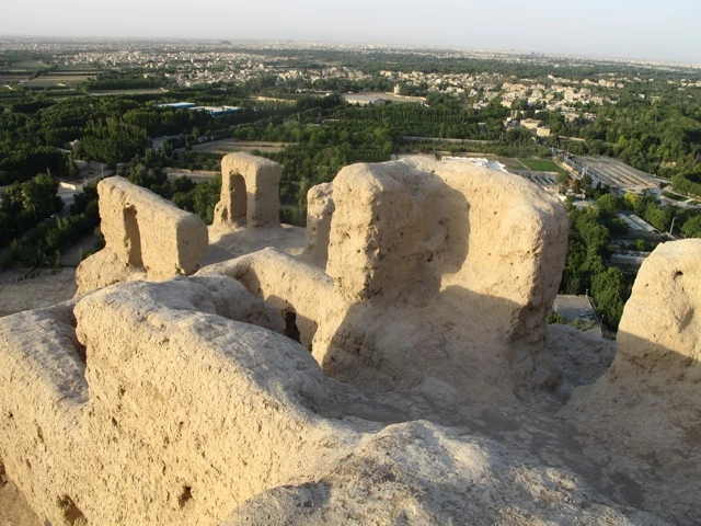 Blick von zerfallenen Lehmbauten auf eine grüne Stadtlandschaft mit Häusern und Bäumen
