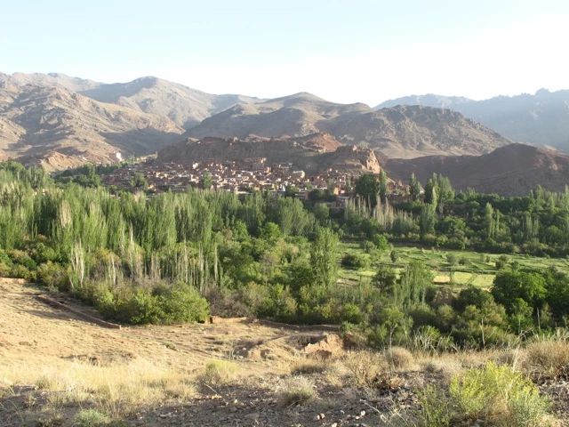 Blick auf ein traditionelles Bergdorf mit roten Häusern, umgeben von grünen Pappeln und felsigen Bergen im Hintergrund