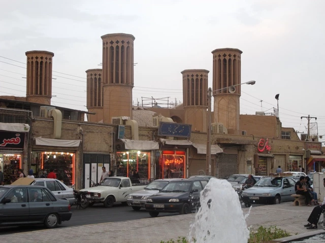 Historische Stadtstraße in Yazd mit traditionellen Windtürmen, Autos und Geschäften vor verschwommener Kulisse