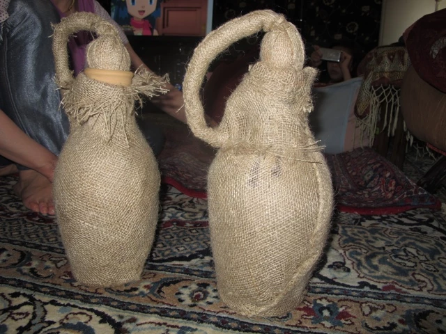 Zwei handgefertigte Puppen aus beigefarbenem Jutestoff mit aufwendiger Kopf- und Körpergestaltung auf gemustertem Teppich