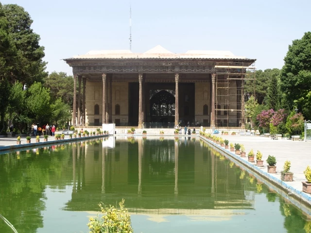 Traditionelles persisches Gebäude mit weißer Säulenfassade und langem grünem Wasserbecken, umgeben von Bäumen