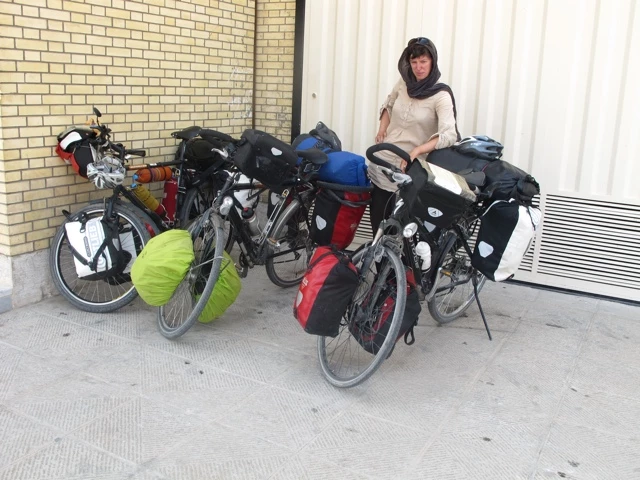 Mehrere beladene Fahrräder mit Satteltaschen, angelehnt an eine gelbe Backsteinmauer und eine weiße Seitenwand