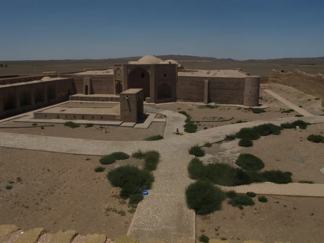 Alte Steinbauwerke mit rechteckigen Gebäuden und Kuppel in trockener Wüstenregion, umgeben von spärlicher Vegetation und Geröll