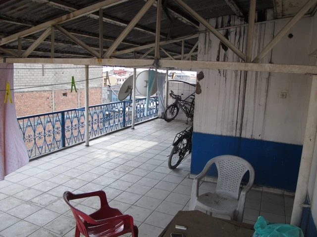 Überdachte Terrasse mit weißen Fliesen, zwei Fahrrädern, zwei Plastikstühlen und blau-weißem Geländer