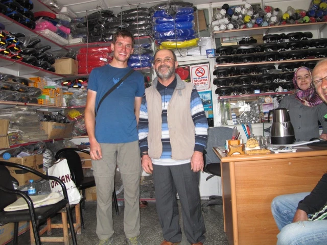 Zwei Männer in einem vollgepackten Ausrüstungsladen mit Regalen voller Taschen und Zubehör, Verkaufstresen im Hintergrund