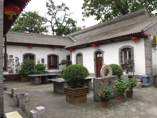 Geräumiger Innenhof mit weißen Mauern, roten Laternen, Ziegelpflaster, Topfpflanzen und Buchsbäumen in einem traditionellen chinesischen Gebäudekomplex