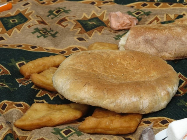 Zwei verschiedene Brote auf einem gemusterten Textil: ein rundes Fladenbrot und ein längliches Brot, daneben goldbraune Gebäckstücke