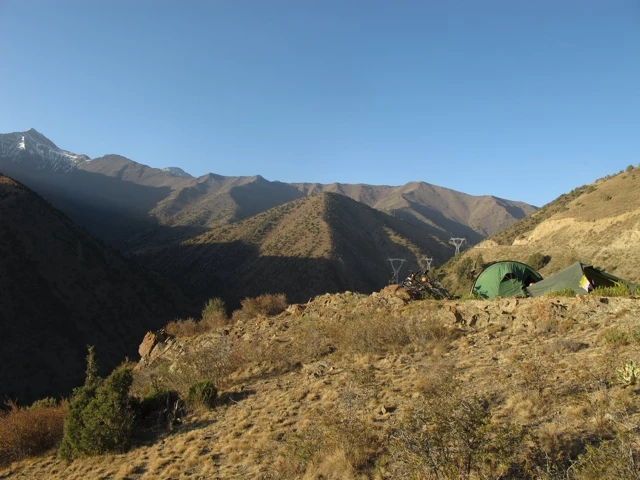 Grüne Zelte auf felsigem Hügel vor weiter Bergkette mit kahlen Hängen und blauem Himmel