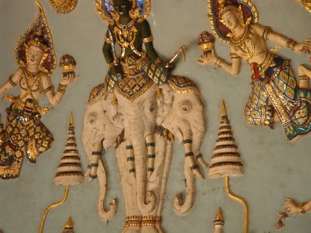 Traditionelle asiatische Kunstdarstellung mit goldverzierten Figuren, eine Gottheit auf einem weißen Elefanten sitzend, umgeben von ornamentalen Elementen