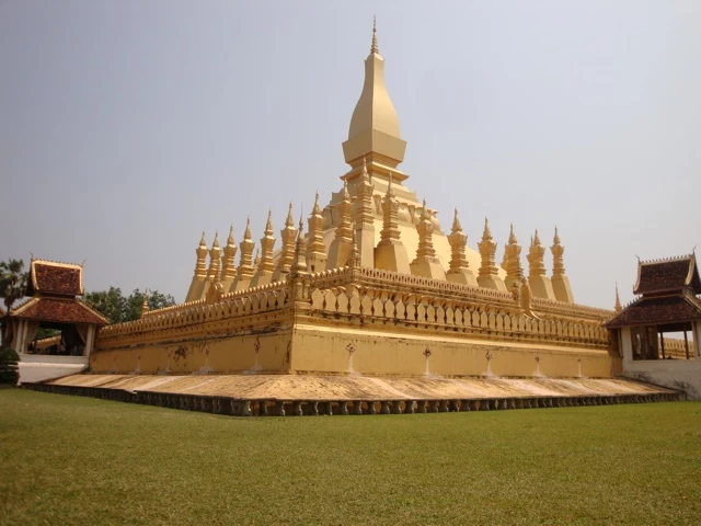 Goldene buddhistische Tempelanlage mit zentraler Stupa und vielen kleineren Türmchen auf grüner Rasenfläche