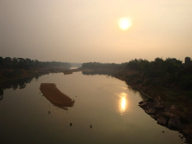 Weiter Fluss mit Sandbänken und Ufervegetation bei gedämpftem Sonnenlicht im Morgengrauen