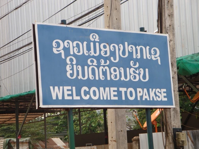 Blaues Willkommensschild mit Schrift auf Laotisch und Englisch: 'Welcome to Pakse'