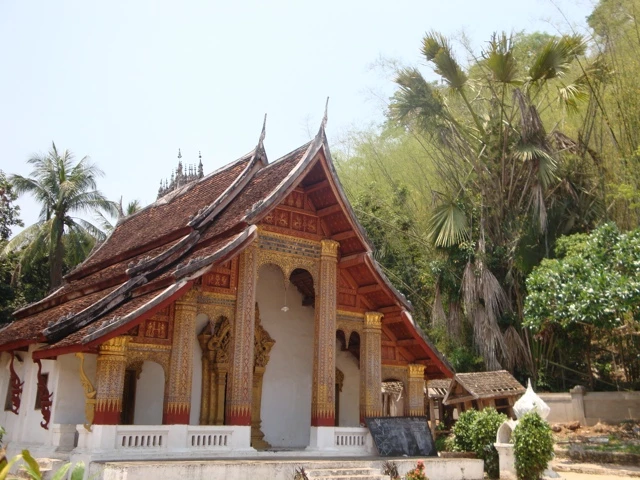 Traditionelles Holztempelgebäude mit geschwungenen Dachlinien, umgeben von Palmen und tropischer Vegetation