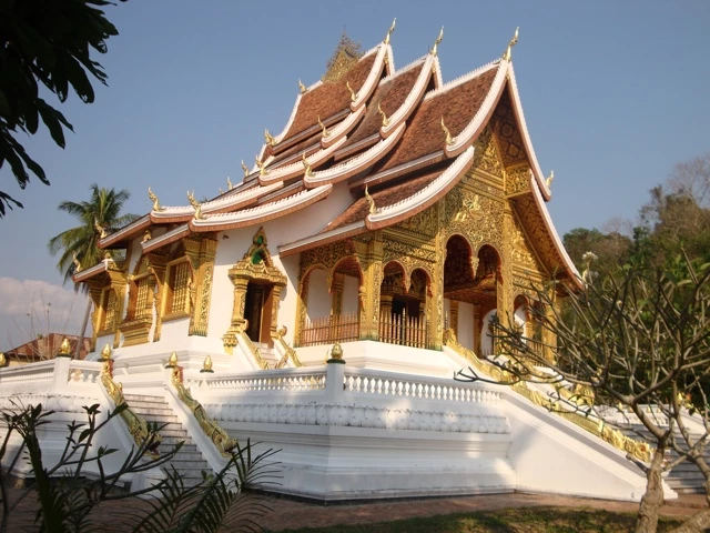 Goldverzierter Tempelbau mit weißem Sockel, geschwungenen Dächern und traditioneller Architektur in Südostasien