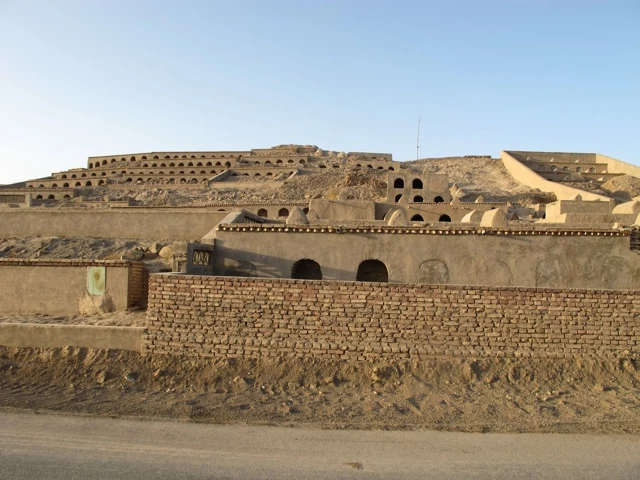 Mehrgeschossige Lehmziegelanlage mit Gewölben und Löchern in trockener Wüstenumgebung, Steinmauer im Vordergrund