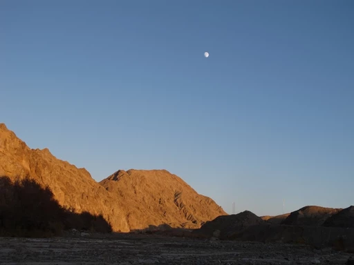 Goldbraune Felsberge in der Abenddämmerung mit Vollmond am klaren blauen Himmel, Wüstenlandschaft im Vordergrund