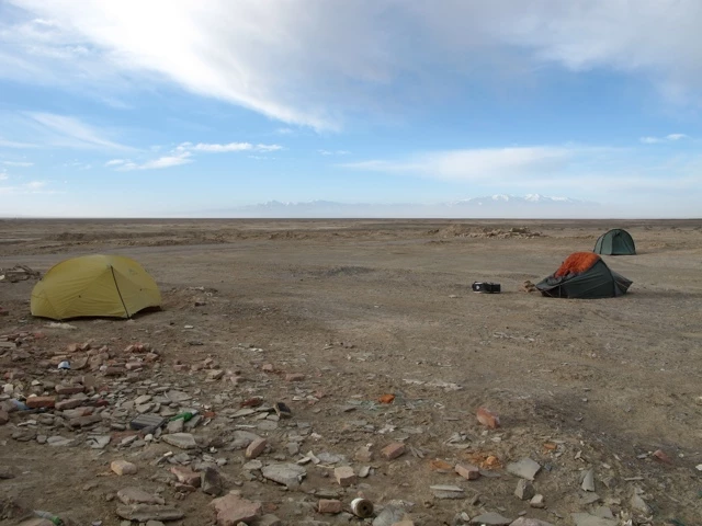 Zwei Zelte in einer steinigen, flachen Wüstenlandschaft - gelbes und orangerotes Zelt auf felsigem Boden mit weitem Horizont