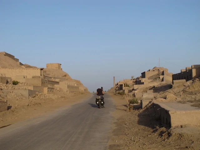Einsame Motorradfahrt durch eine verlassene Lehmstadt in der Taklamakan-Wüste, staubige Straße zwischen verfallenen Gebäuden