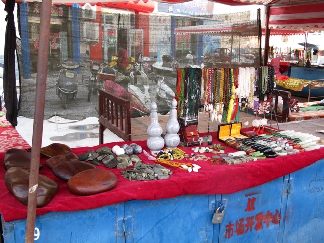 Bunter Marktstand mit roter Decke, verschiedene Steine, Halsketten und Schmuckstücke, im Hintergrund Marktatmosphäre